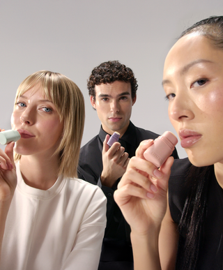 Two women and a man posing together, each holding a refillable lip balm near their lips to showcase a shared, sustainable skincare routine.