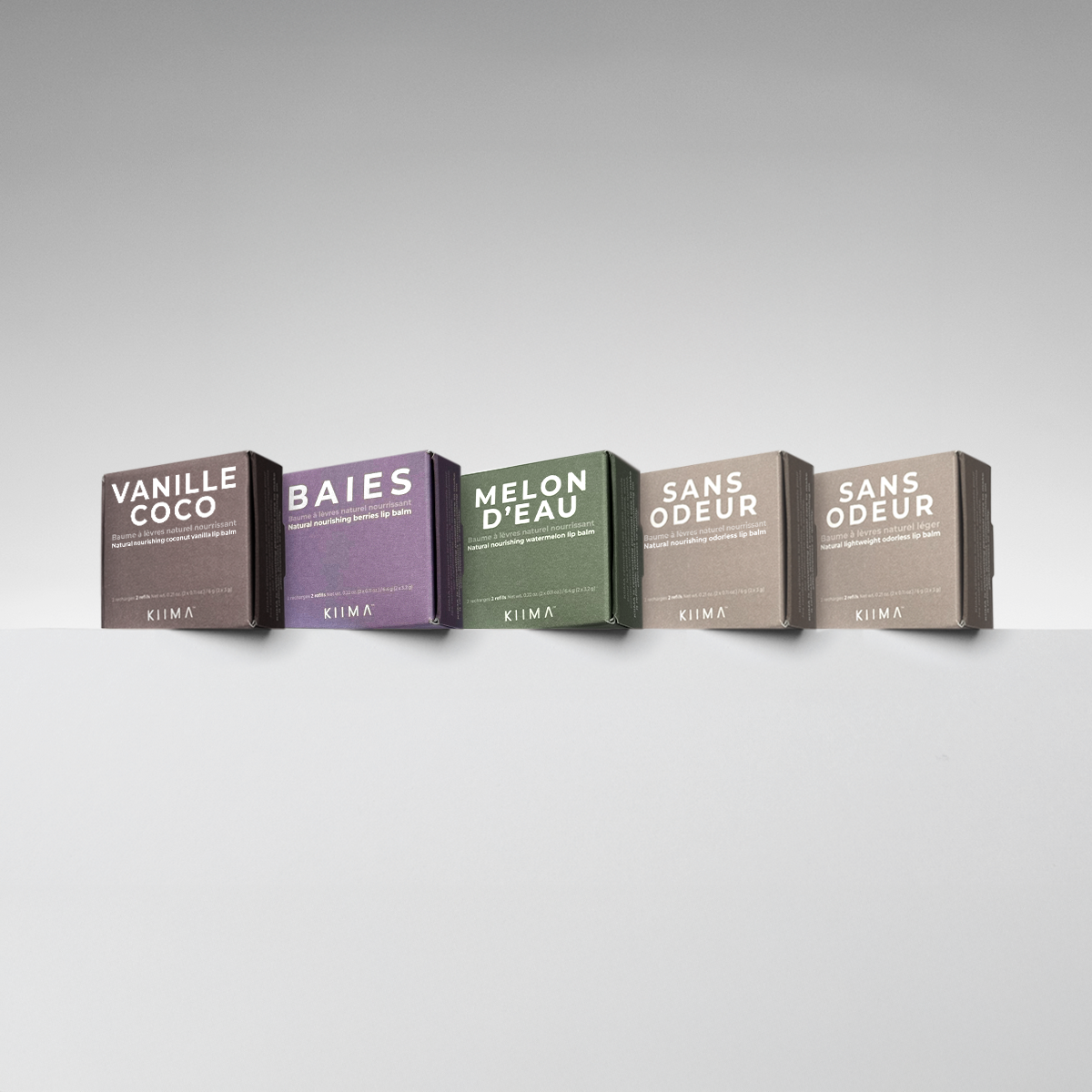 Five lip balm boxes with different scents on a gray background