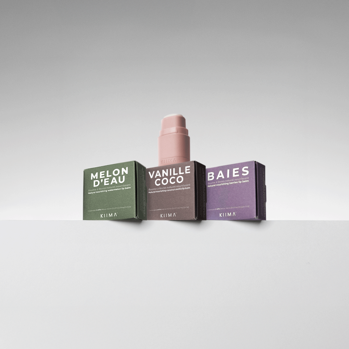 Close-up GIF of a pink KIIMA refillable lip balm applicator opening in front of Melon d’Eau, Vanille Coco, and Baies refill boxes.