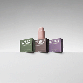 Close-up GIF of a pink KIIMA refillable lip balm applicator opening in front of Melon d’Eau, Vanille Coco, and Baies refill boxes.
